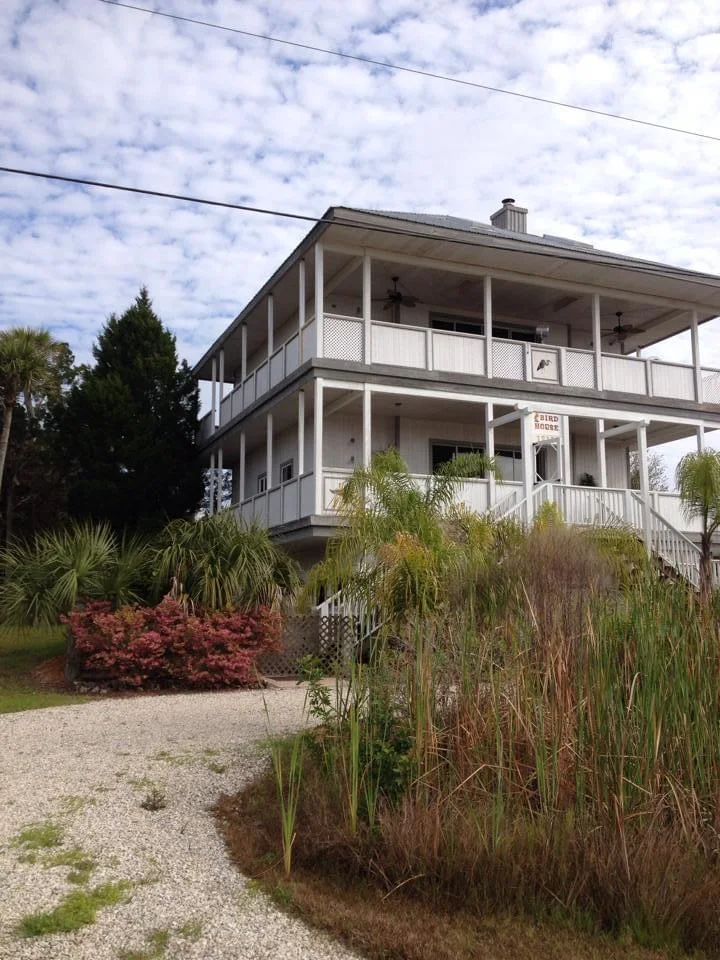 View of a coastal-style home in Crystal River, Florida, with a freshly painted white exterior with gray accents, featuring double balconies with white railings and lattice work, showcasing expert painting by T&B Paint Pros.